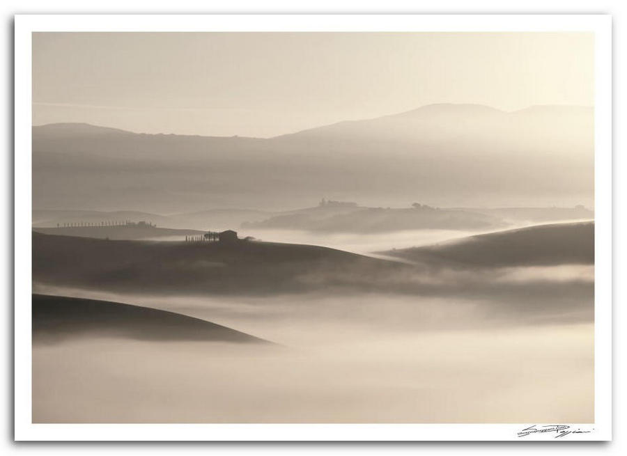 Fotografia artistica di Silvano Poggiani raffigurante il paesaggio della campagna toscana vicino Pienza, Siena. Paesaggio collinare all'alba con nebbia che avvolge le valli, casolare e morbide ondulazioni del terreno in controluce.