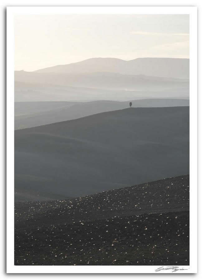 Fotografia artistica di Silvano Poggiani raffigurante il paesaggio della campagna toscana vicino Pienza, Siena. Colline scure si susseguono come onde di terra, sfumando in tonalità sempre più tenui fino a dissolversi nella foschia dell’alba.