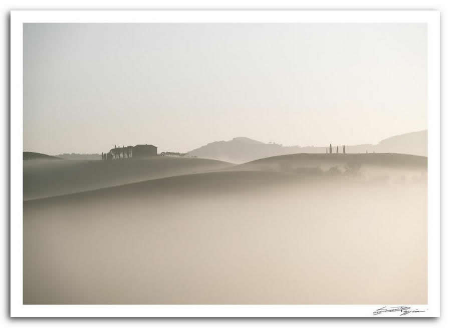 Fotografia artistica di Silvano Poggiani raffigurante il paesaggio della campagna toscana vicino Pienza, Siena. Paesaggio collinare avvolto nella nebbia con una casa e alberi sullo sfondo.